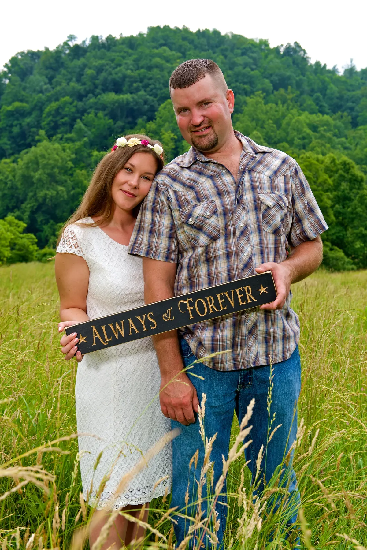 Couple standing in a meadow holding an Always and Forever sign