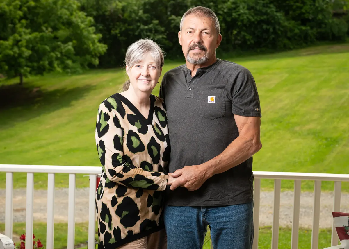 Couple holding hands beside a white railing with a green lawn behind them
