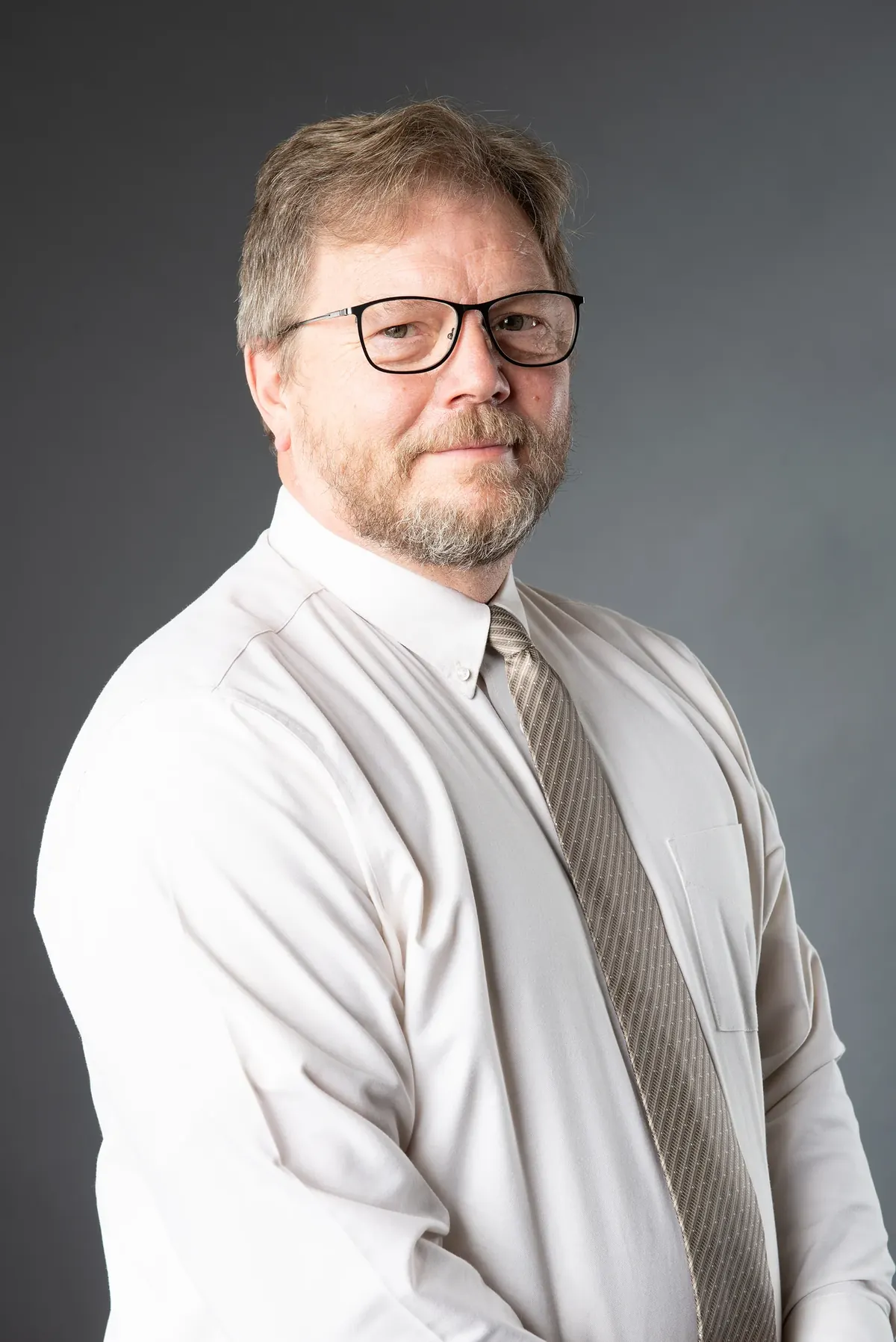 Man wearing glasses, a white shirt and tie against a gray background