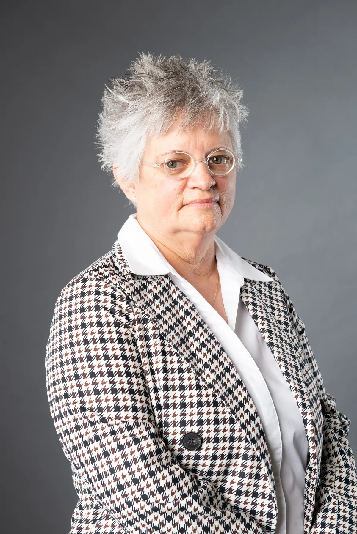 Woman wearing glasses and a checked blazer against a gray background