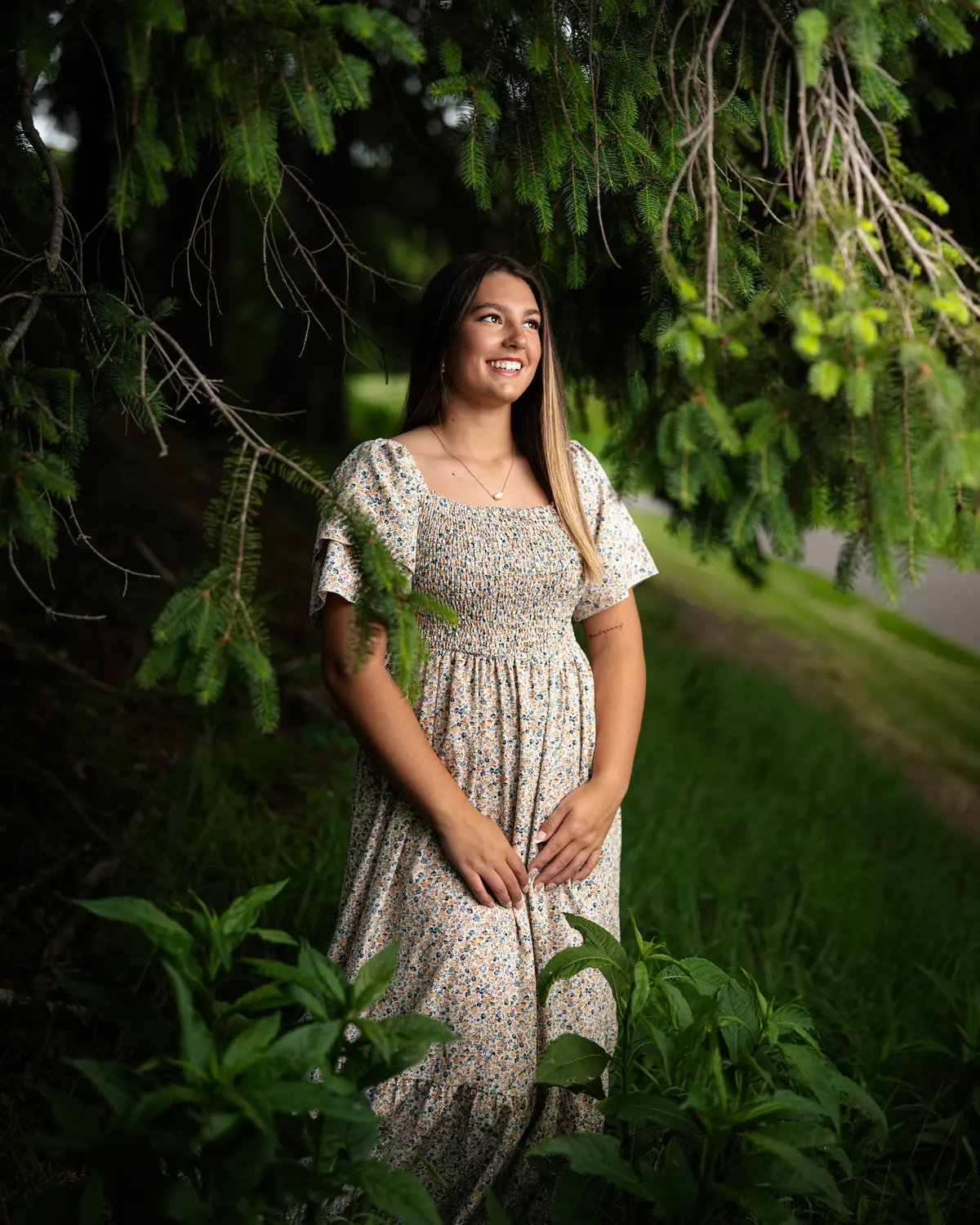 Senior portrait in a patterned dress beneath lush green branches