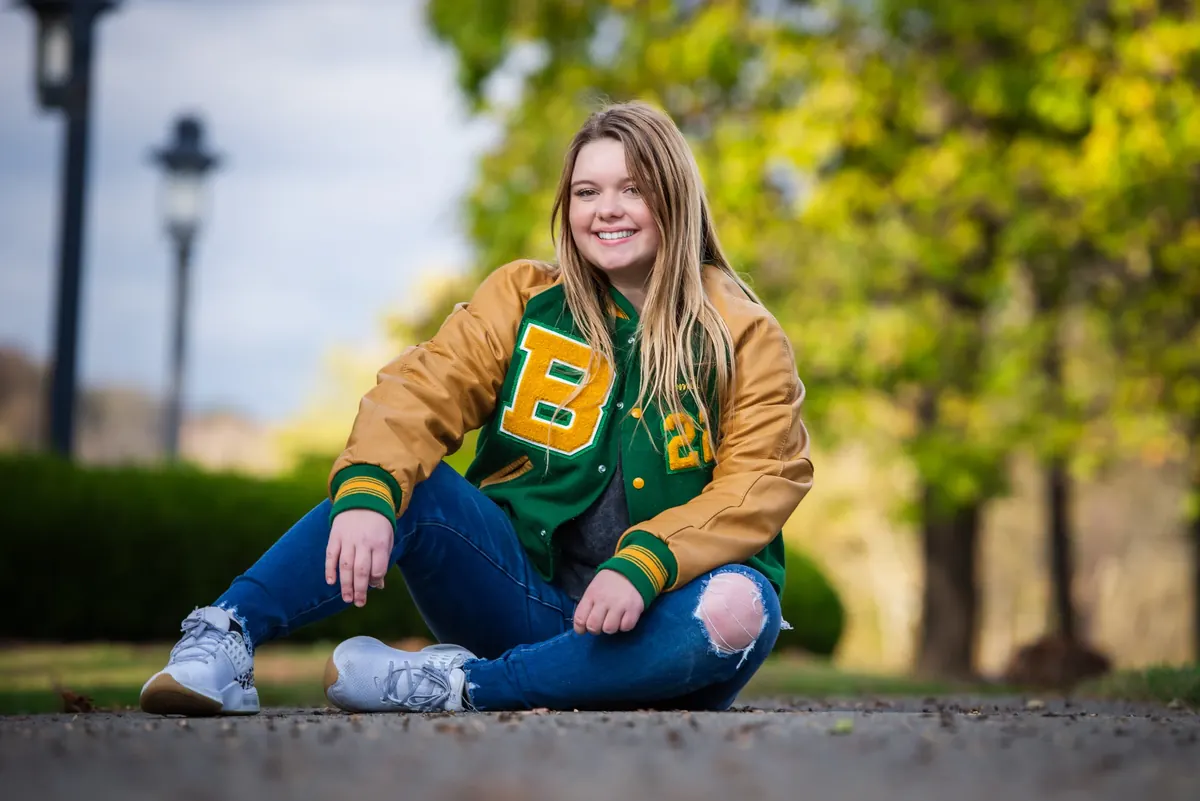Senior seated outdoors in a green and gold letterman jacket