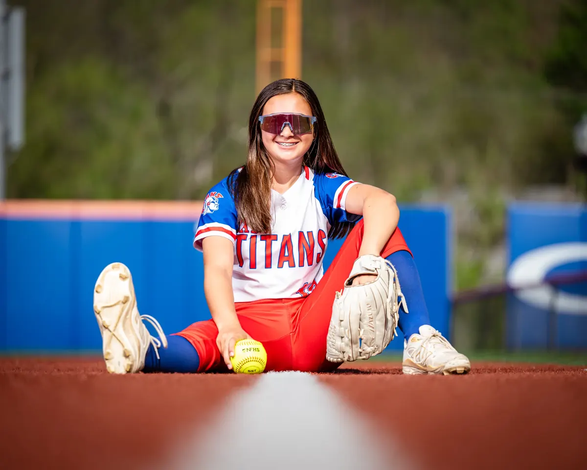 Softball player seated on the field with a glove and softball
